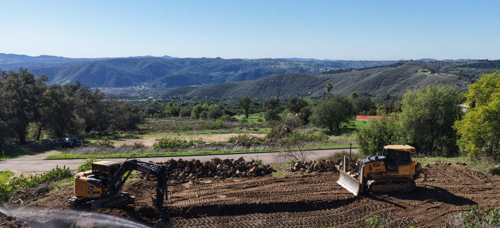 Excavator and bulldozer clearing land with a scenic mountain valley backdrop, Sovereignty Construction performing site development work across complex Western terrain.