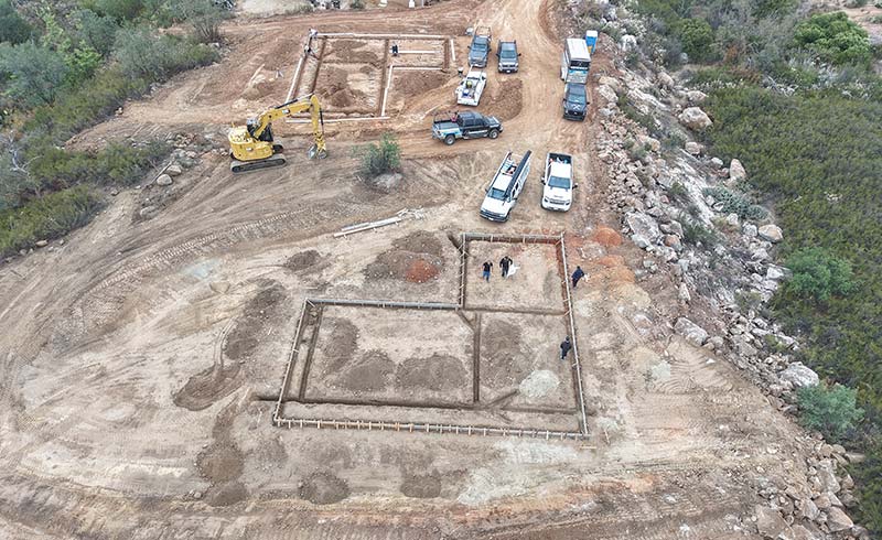 Aerial view of a home foundation being laid with excavation equipment and trucks on site, a Sovereignty Construction home project.
